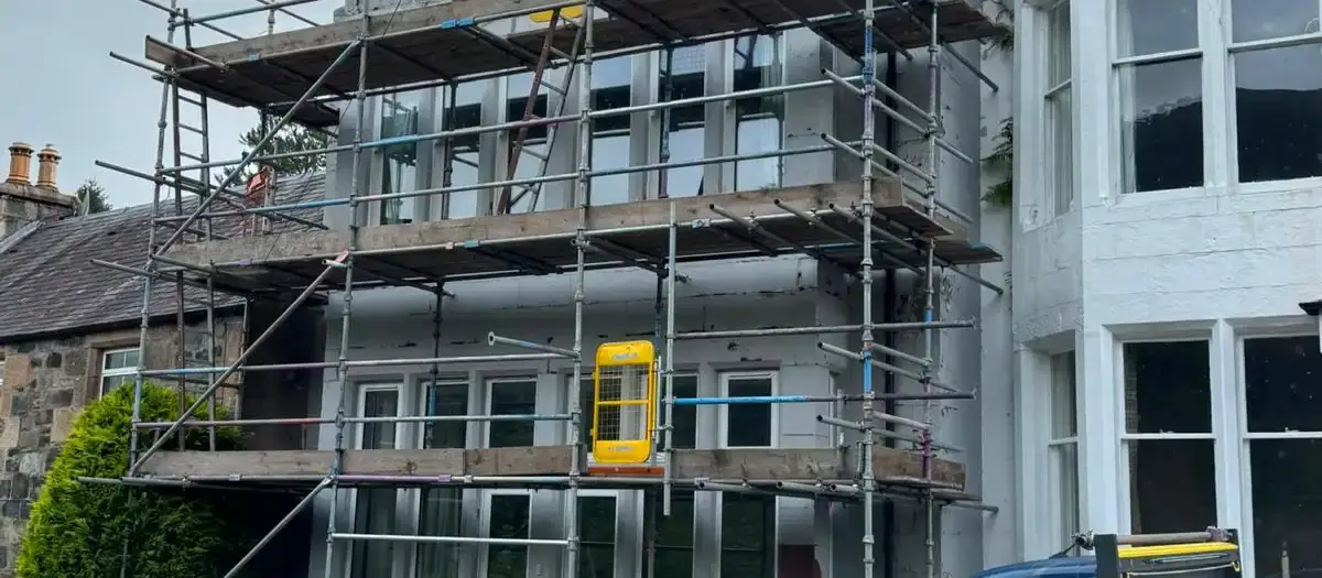 Scaffolding across the front of a white-painted house, with the firm’s van parked outside